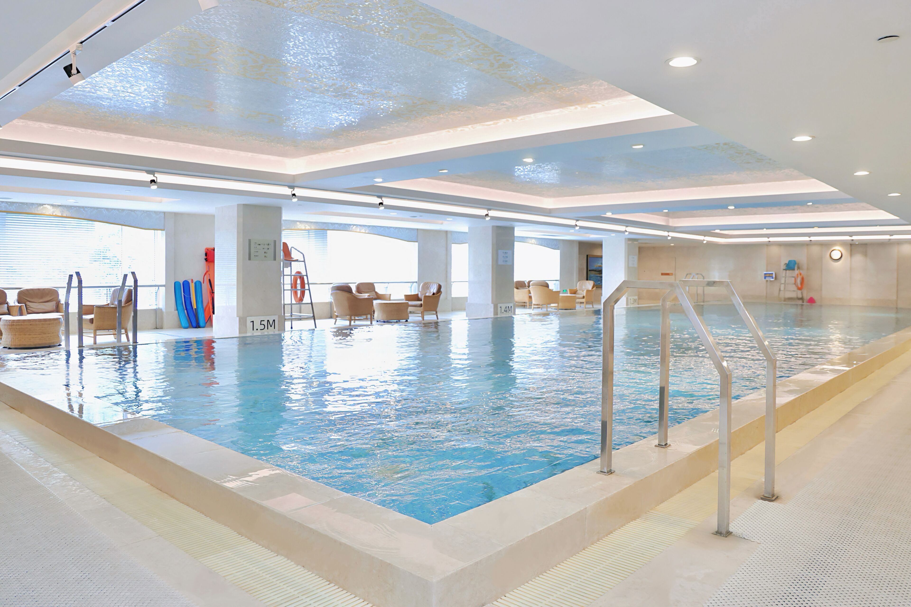 Piscina interior con agua cristalina, rodeada de sillones de descanso y una cama solárium.