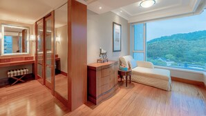 A hotel room with a large window, wooden flooring, a wardrobe, a bedside table with a lamp, and a view of a forested area. - The Dragon Hotel (Hangzhou)
