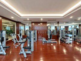 Un gimnasio moderno con diversas máquinas de ejercicio, suelo de madera y un muro con espejos.