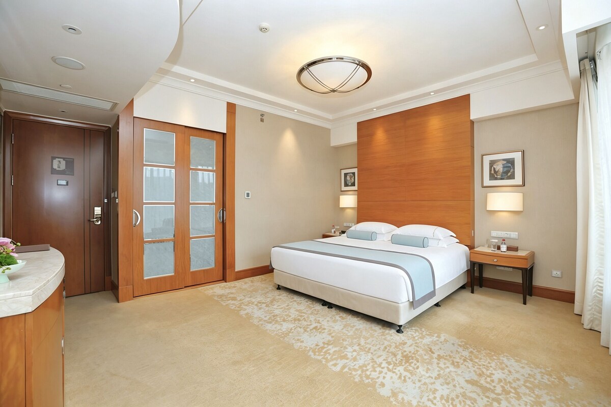 A hotel room with a bed, a desk, a nightstand, a wooden wardrobe, and a bathroom door.