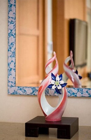 Eine dekorative Glasvase mit floralem Dekor auf dunklem Sockel, vor einem Spiegel mit blau-weiß gemusterten Rahmen platziert.