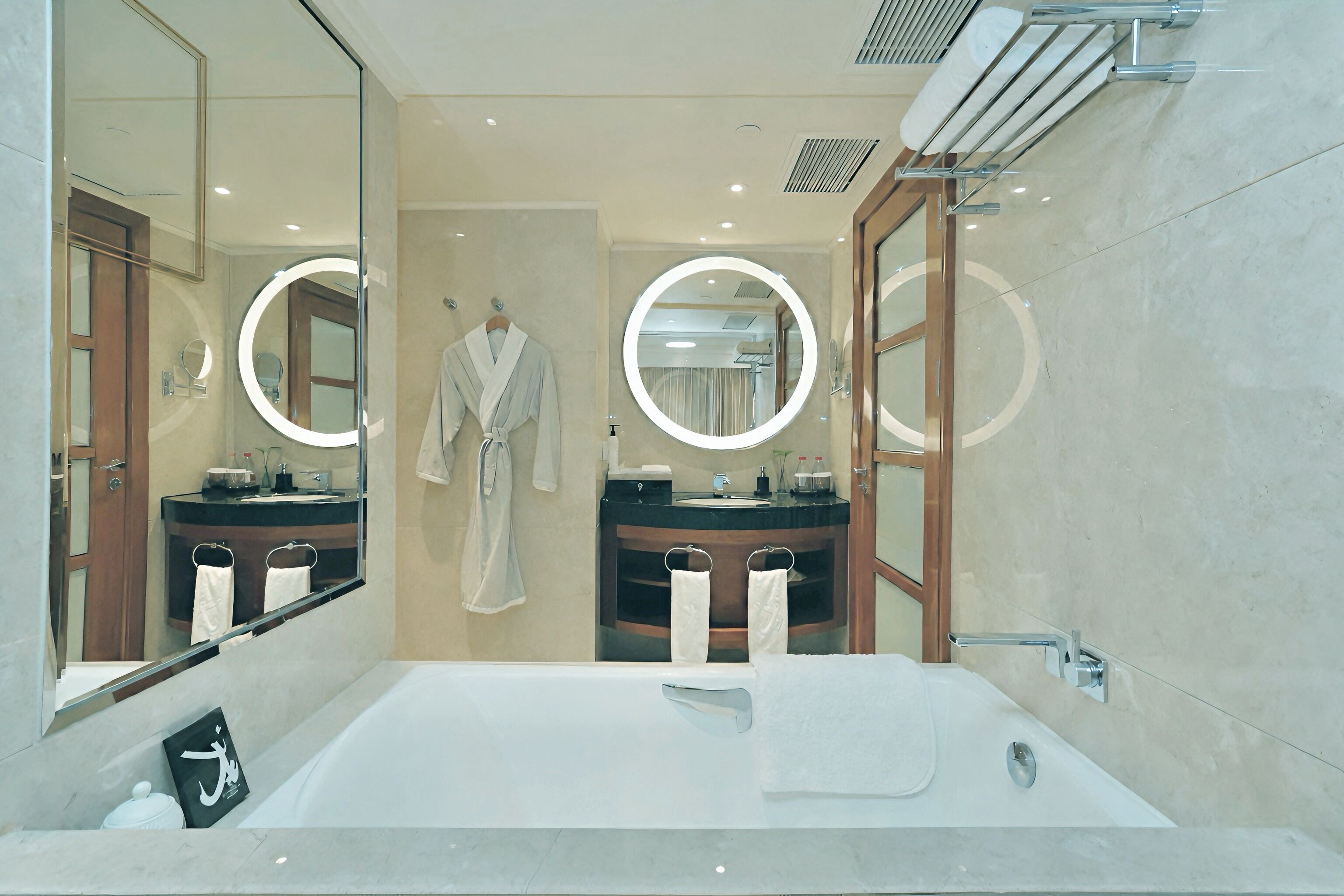 A modern bathroom with a large bathtub, two sinks, and a robe hanging on the wall.