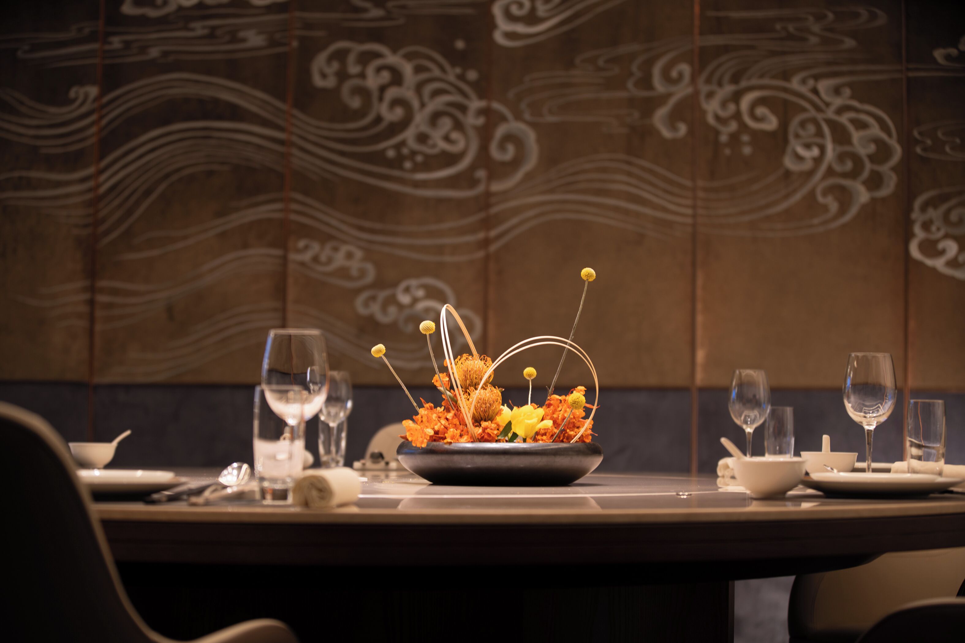 Una mesa de comedor dispuesta con platos, vasos y un centro de mesa con flores.