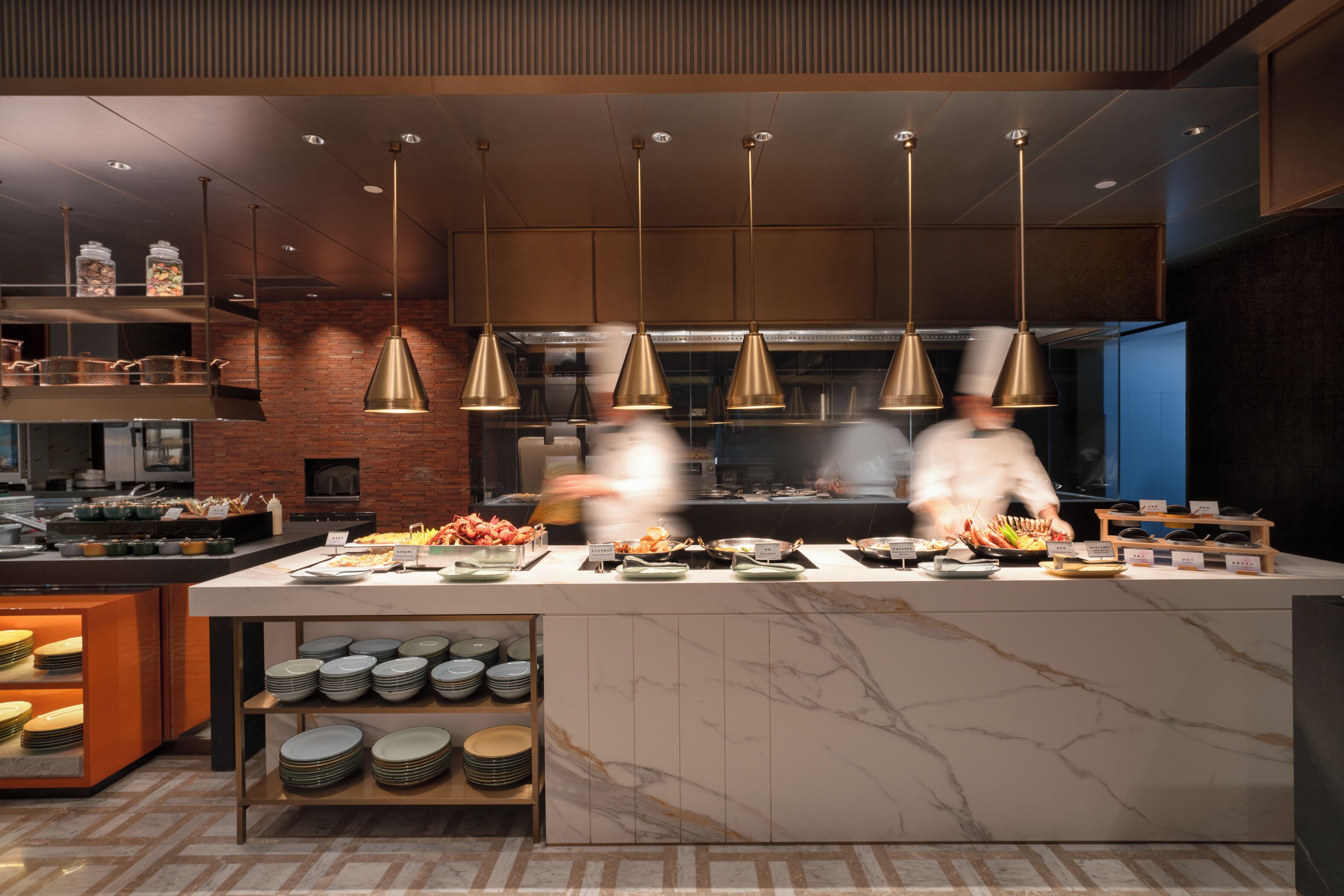 A modern kitchen with a marble countertop, hanging pendant lights, and a brick wall.