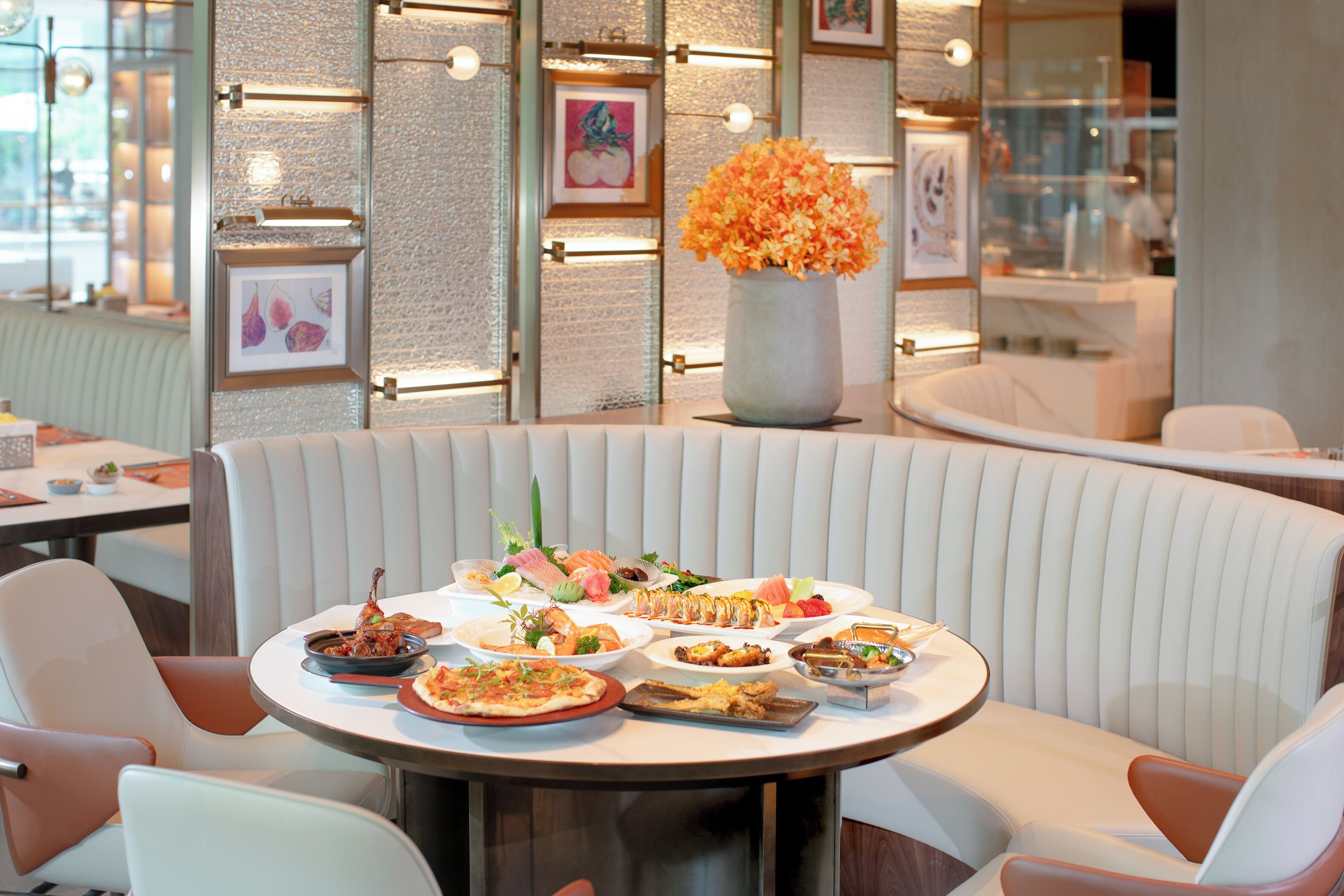 A restaurant interior with a round table set for a meal, cushioned seating, and framed artwork on the walls.