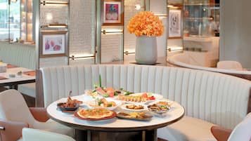 A restaurant interior with a round table set for a meal, cushioned seating, and framed artwork on the walls.