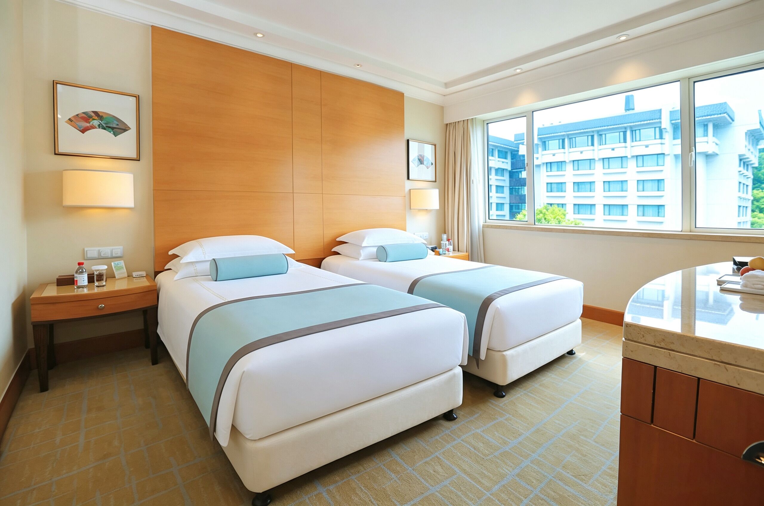 A hotel room with two beds, a wooden headboard, a large window with a city view, and a small bedside table with a lamp.