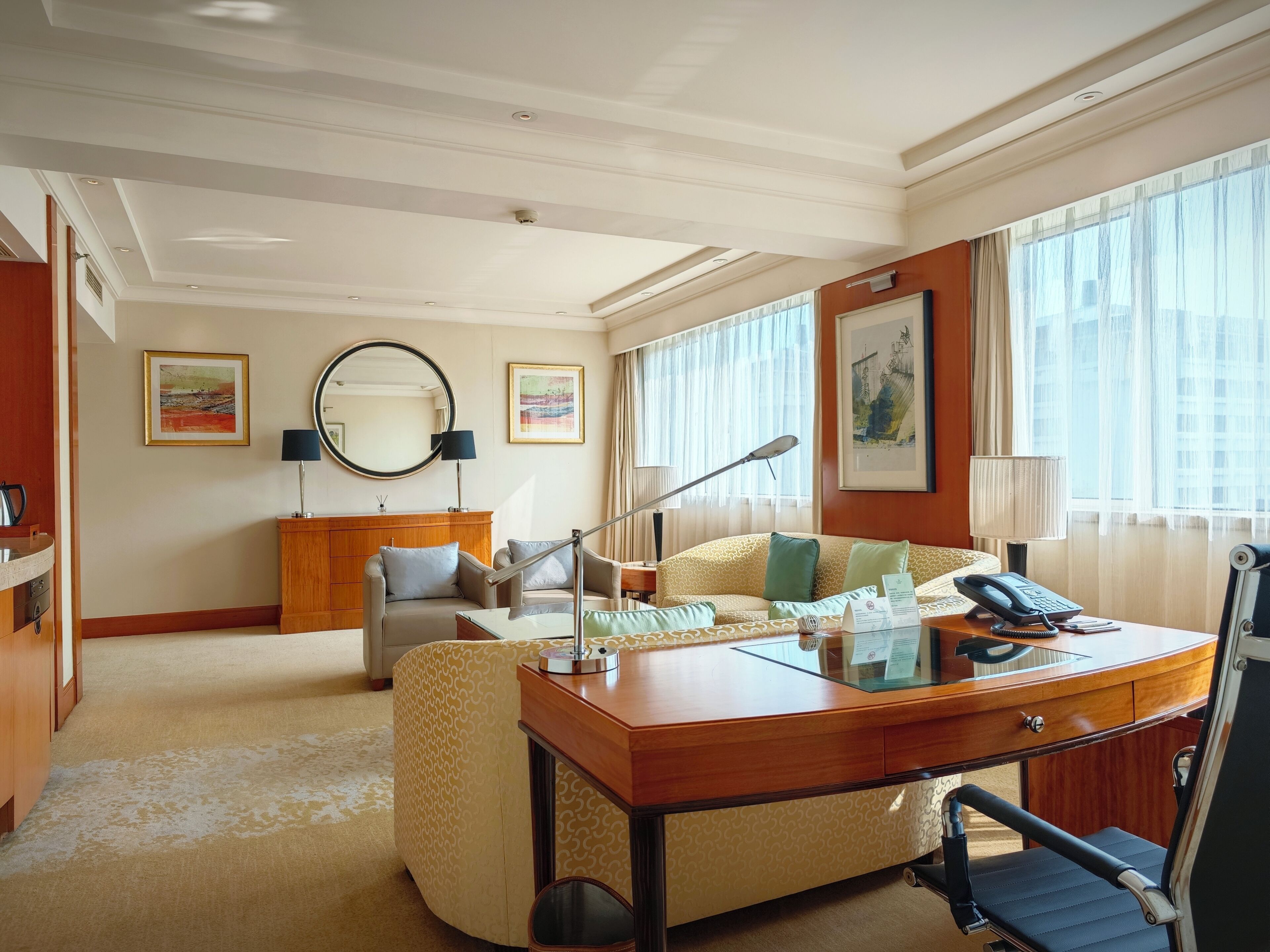 Habitación de hotel con un escritorio de madera, un sofá, un espejo grande y vistas a la ciudad a través de la ventana.