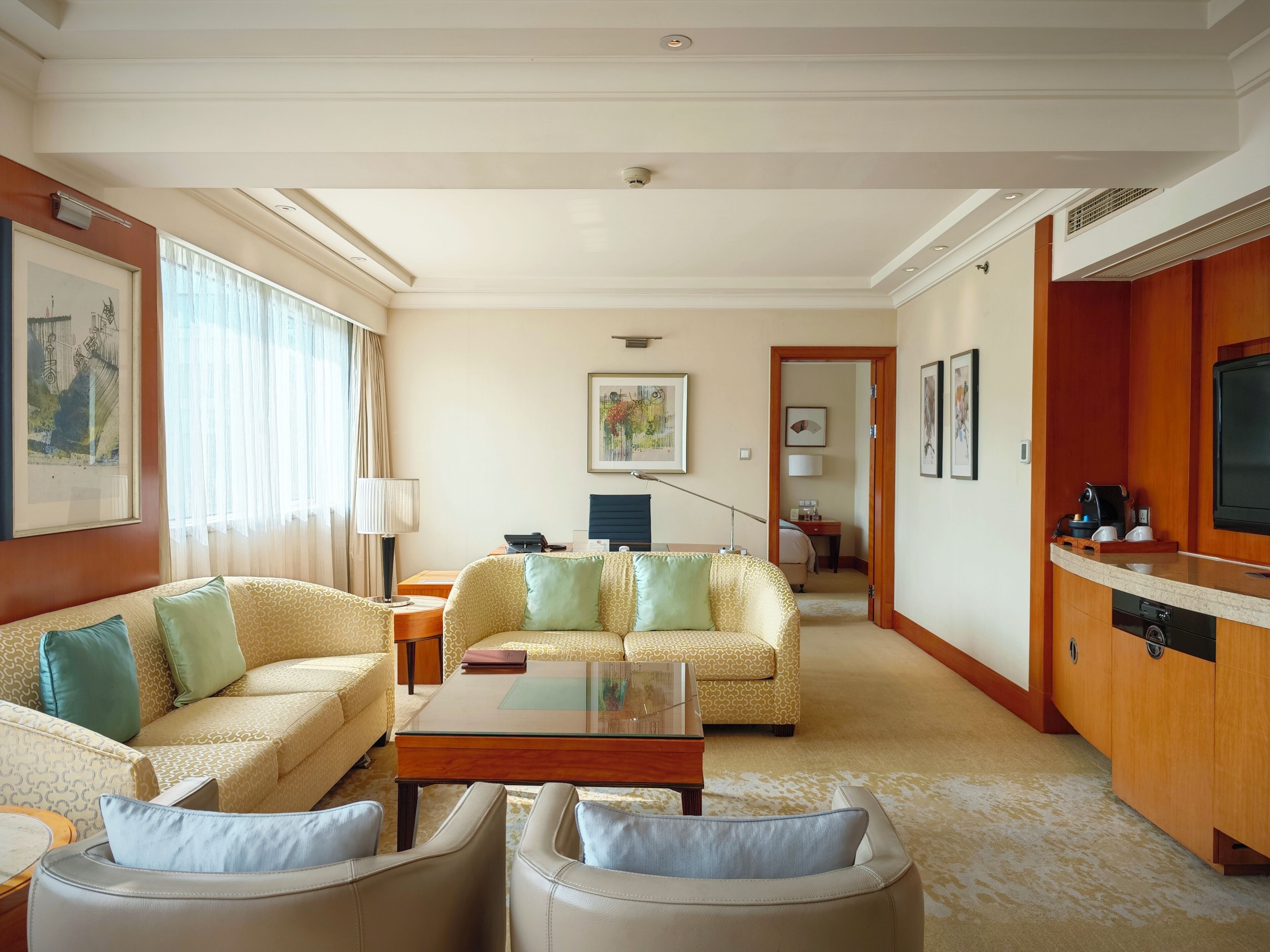 A hotel room with a sofa set, a coffee table, a TV, and a kitchenette area.