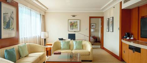 A hotel room with a sofa set, a coffee table, a TV, and a kitchenette area.