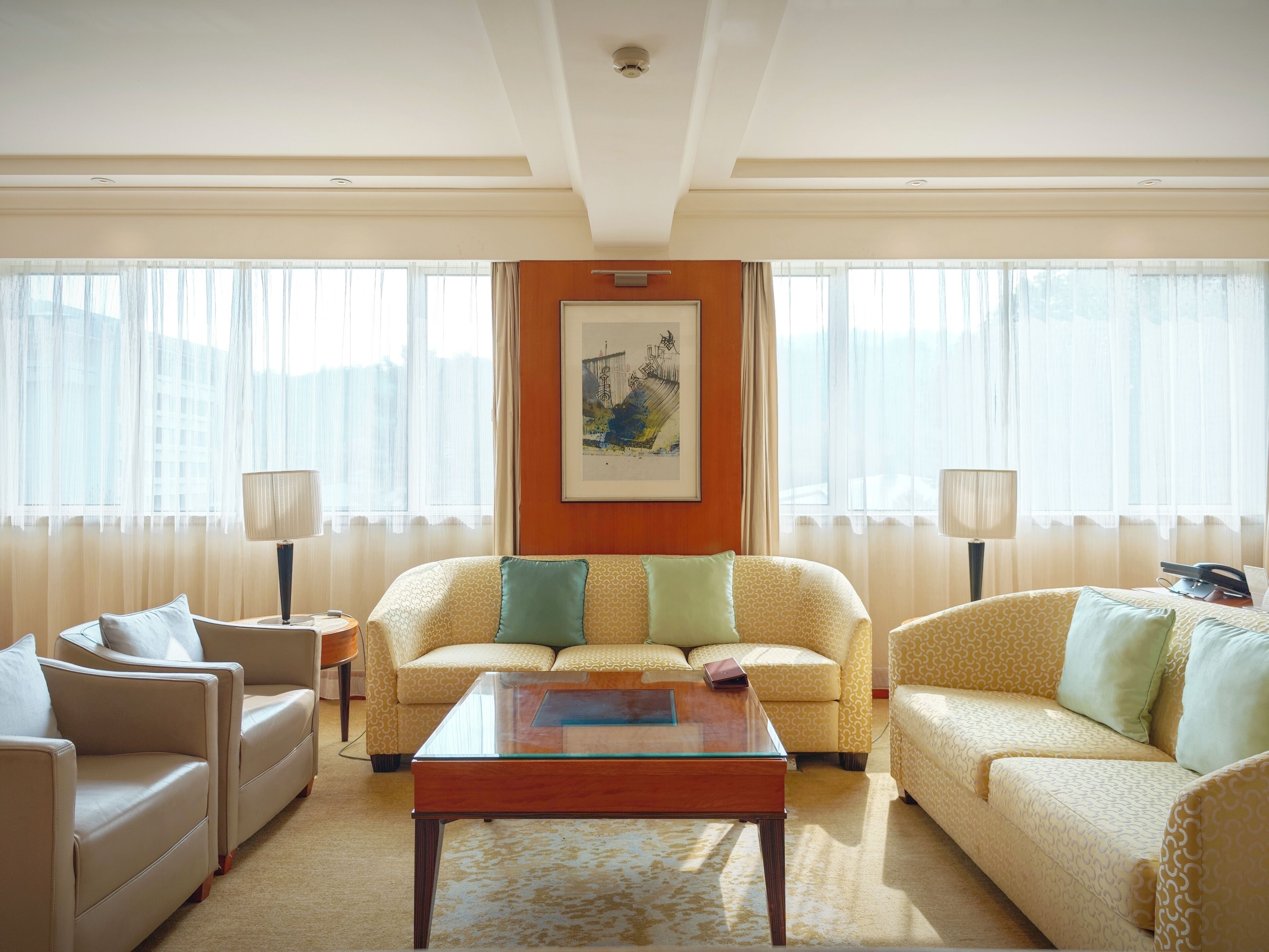 A hotel room with a sofa set, a glass coffee table, and a framed picture on the wall.