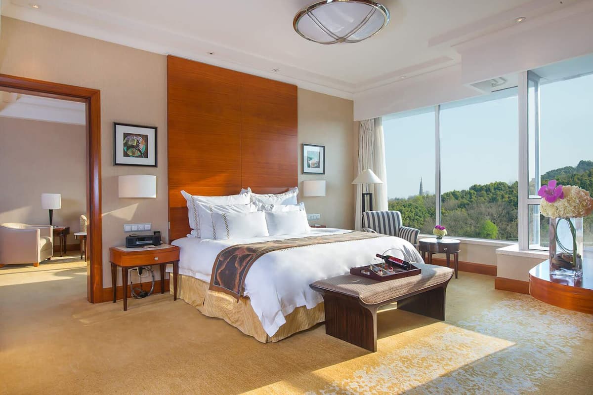 A spacious hotel room with a large bed, a sitting area, and a view of the outdoors.