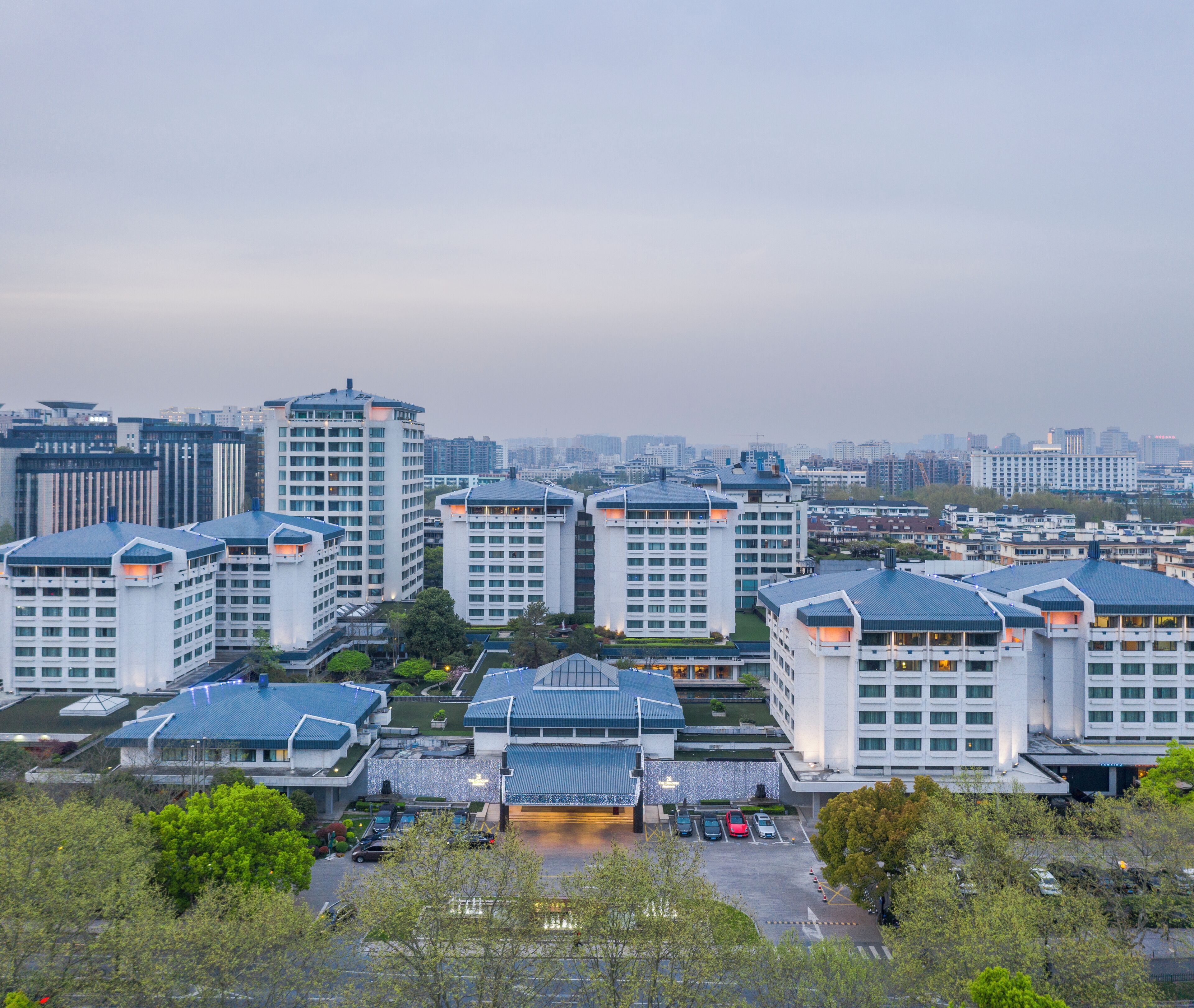 A high-rise hotel complex with multiple buildings, a parking area, and surrounding greenery.