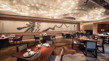 A modern dining area with multiple tables, chairs, and a large abstract painting on the wall.