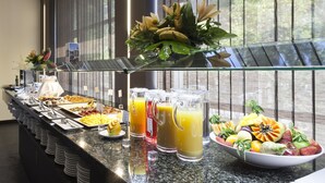 A buffet with various food items and beverages, a decorative plant arrangement, and a window view.