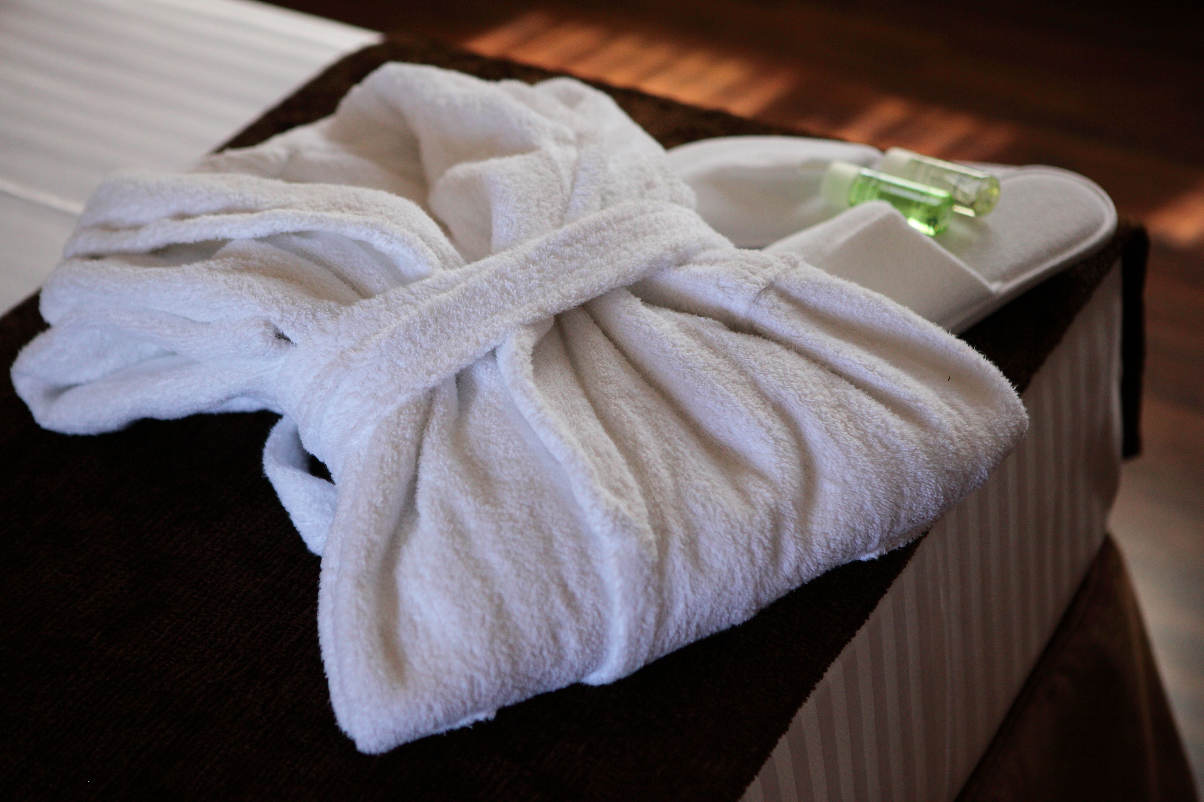 A neatly folded white bathrobe on a wooden surface with a bottle of lotion.