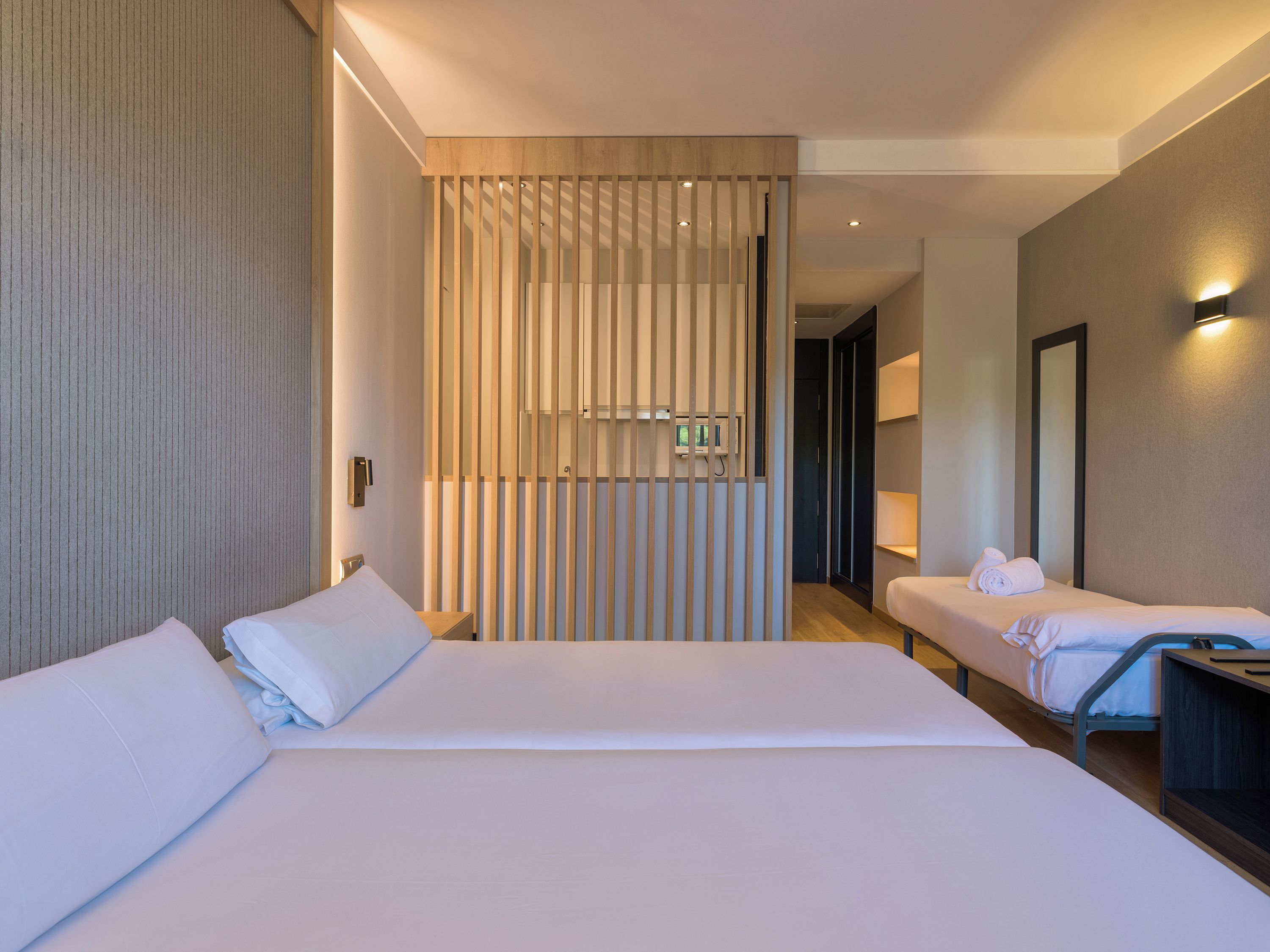 Habitación de hotel con dos camas, un separador de madera, un televisor y un espejo.