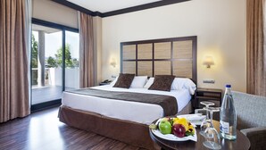 A hotel room with a large bed, a dining table with fruit and glasses, and a view of the outdoors.