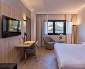 Een hotelkamer met een bed, een bureau met stoel, een televisie, een raam met gordijnen en een kleine tafel met een plant.