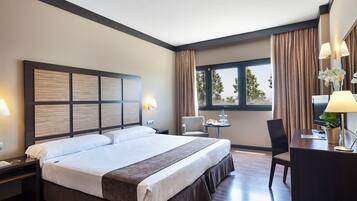 Een hotelkamer met een groot bed, een bureau met stoel, een kleine tafel en een raam met gordijnen.