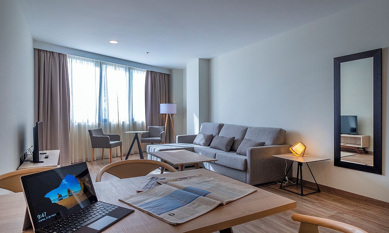 Une chambre d’hôtel moderne équipée d’un canapé, d’une table basse, d’un ordinateur portable et d’une lampe.