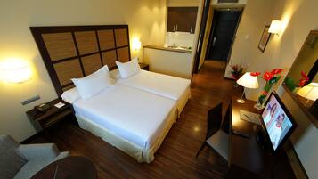 A hotel room with a large bed, a desk with a TV, a chair, a nightstand, and a small kitchenette area.
