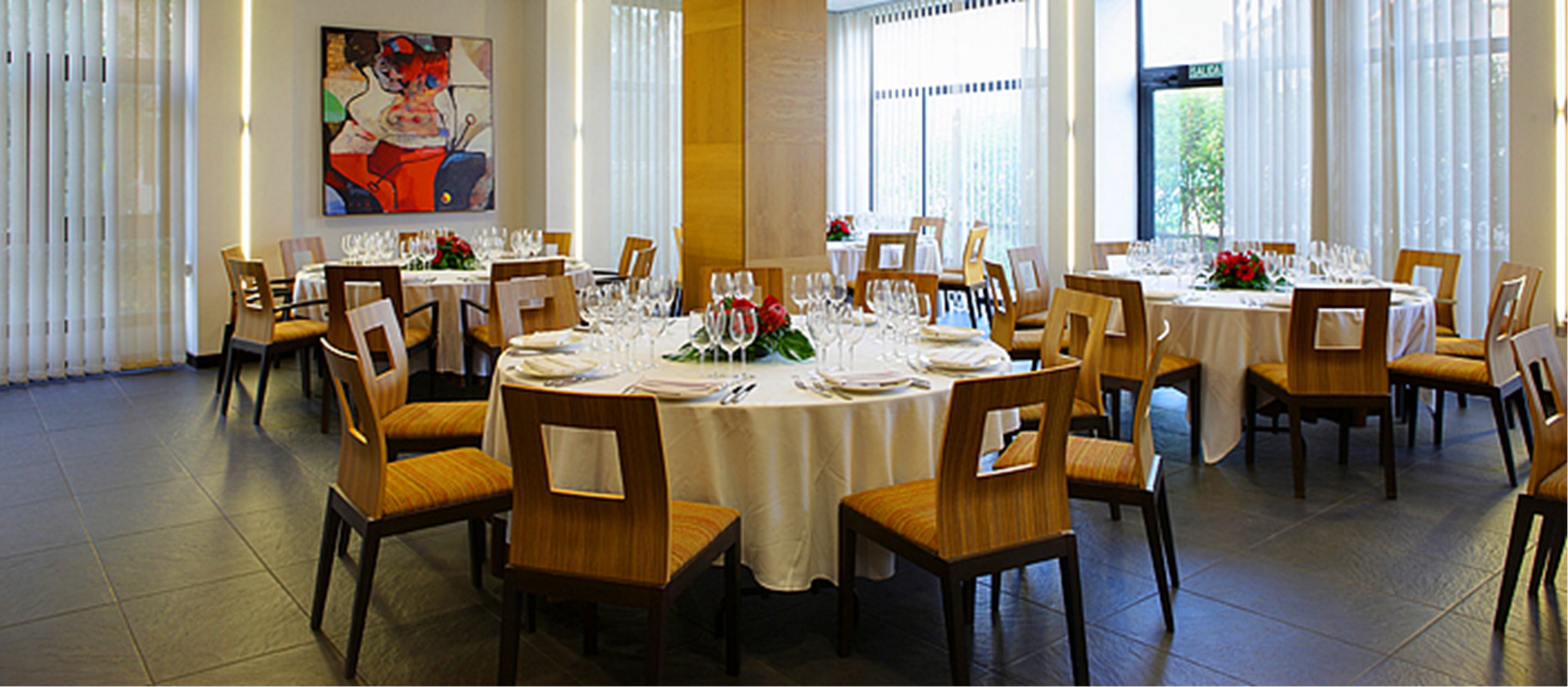 A dining area with round tables set for four, each with white tablecloths, chairs, and glassware.