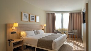 A hotel room with a large bed, bedside lamps, a desk, a chair, and a TV on the wall.