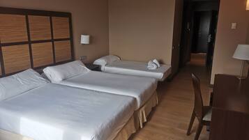 A hotel room with two beds, a desk, a chair, and a door leading to another room.