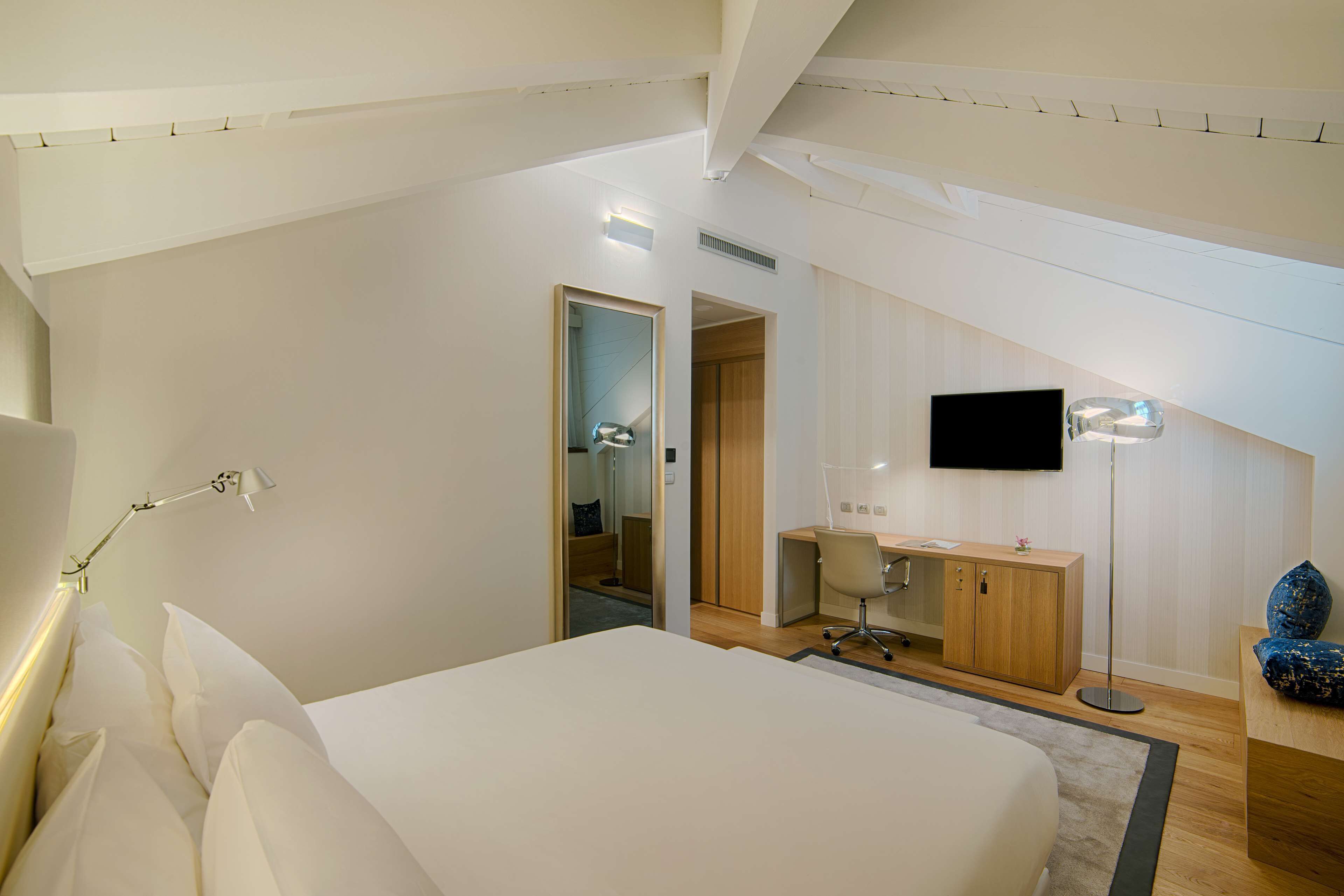 A modern bedroom with a large bed, a desk, a chair, a TV, and a wardrobe.