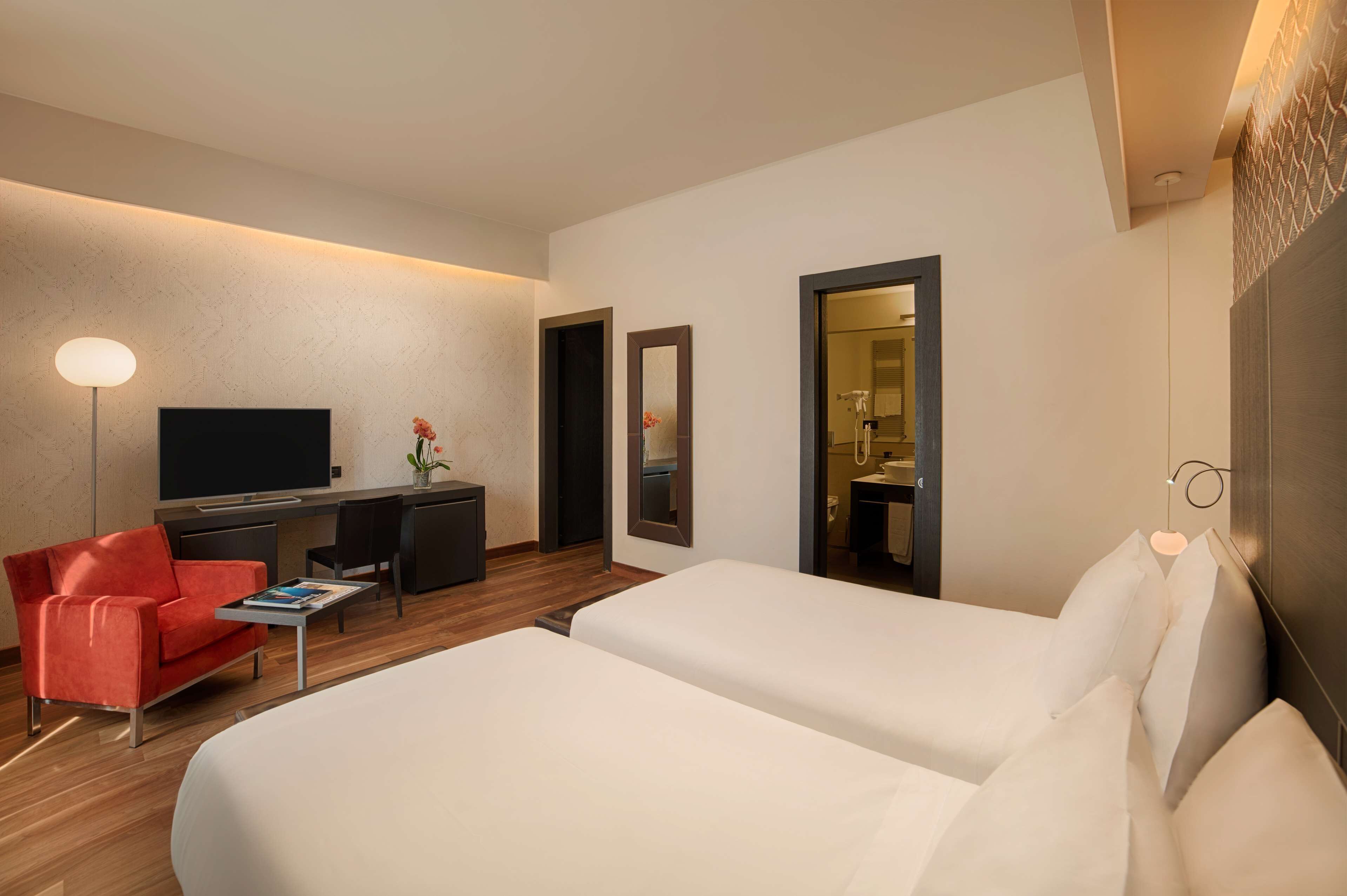 A hotel room with a bed, a desk, a chair, a TV, and a mirror.