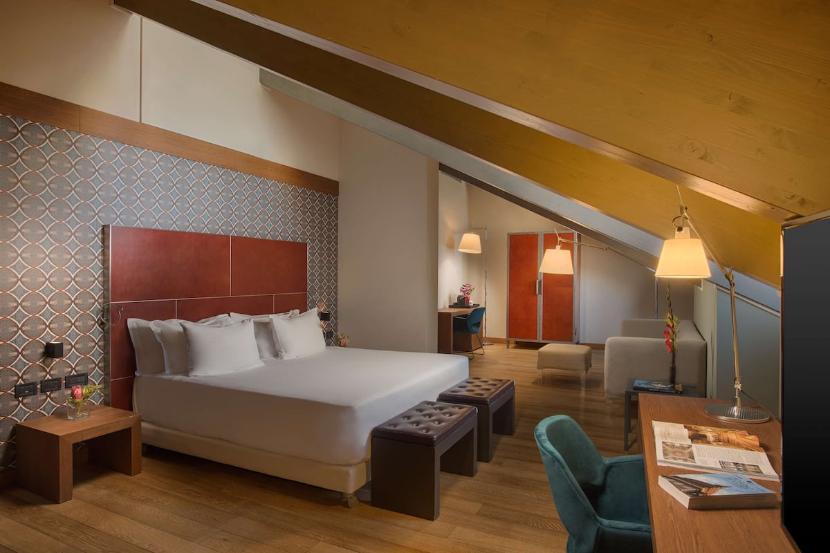 Ein modernes Hotelzimmer mit einem großen Bett, Holzboden und einem Schreibtisch mit Lampe.