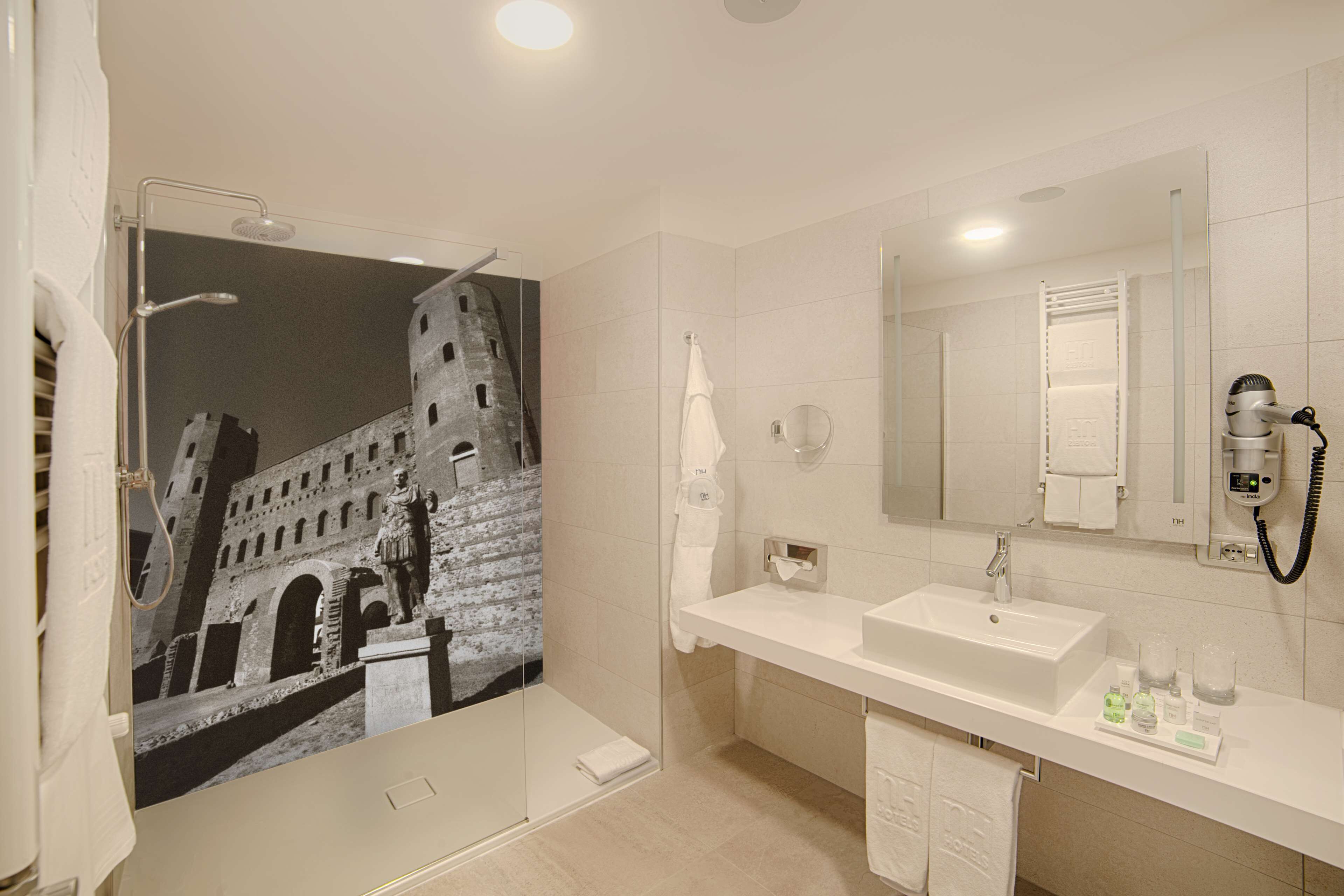 A modern bathroom with a large mirror, a shower with a glass door, and a sink with toiletries.