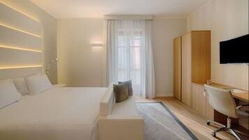 A modern hotel room with a large bed, a sitting area, a desk, and a TV.