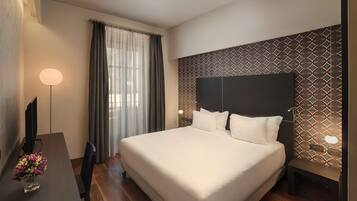 A modern hotel room with a large bed, a desk with a lamp, and a TV.