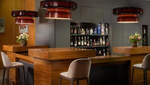 A bar area with wooden bar counters, two bar stools, and hanging pendant lights. - NH Collection Torino Santo Stefano (Turin)
