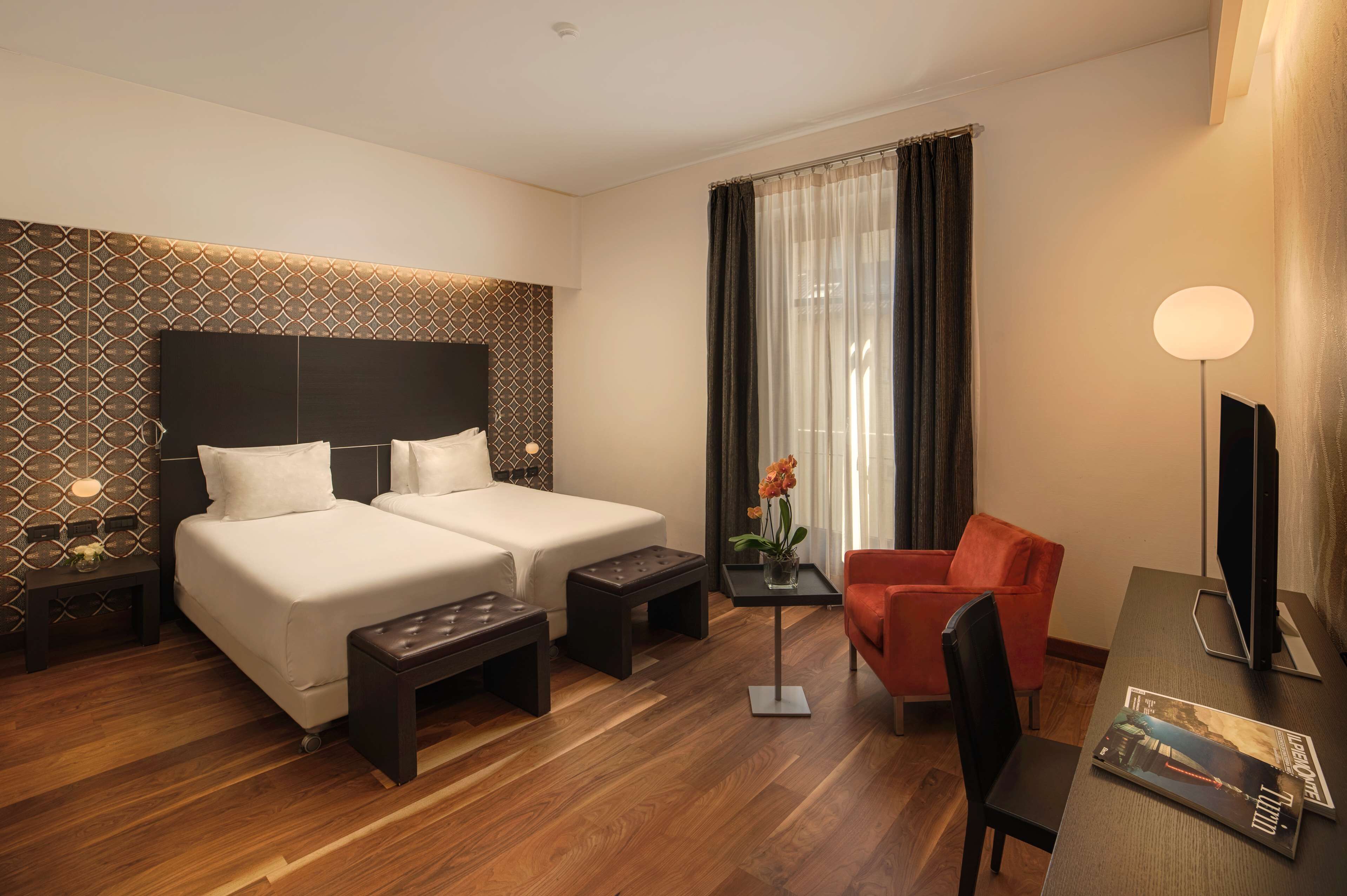 A hotel room with two beds, a desk with a chair, a small table with a vase, and a TV.