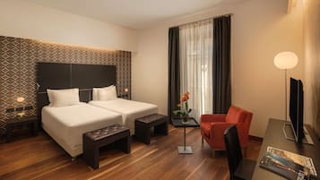 A hotel room with two beds, a desk with a chair, a small table with a vase, and a TV.