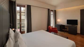 Una camera d'albergo con un letto grande, una scrivania e una TV, e un balcone con tende.