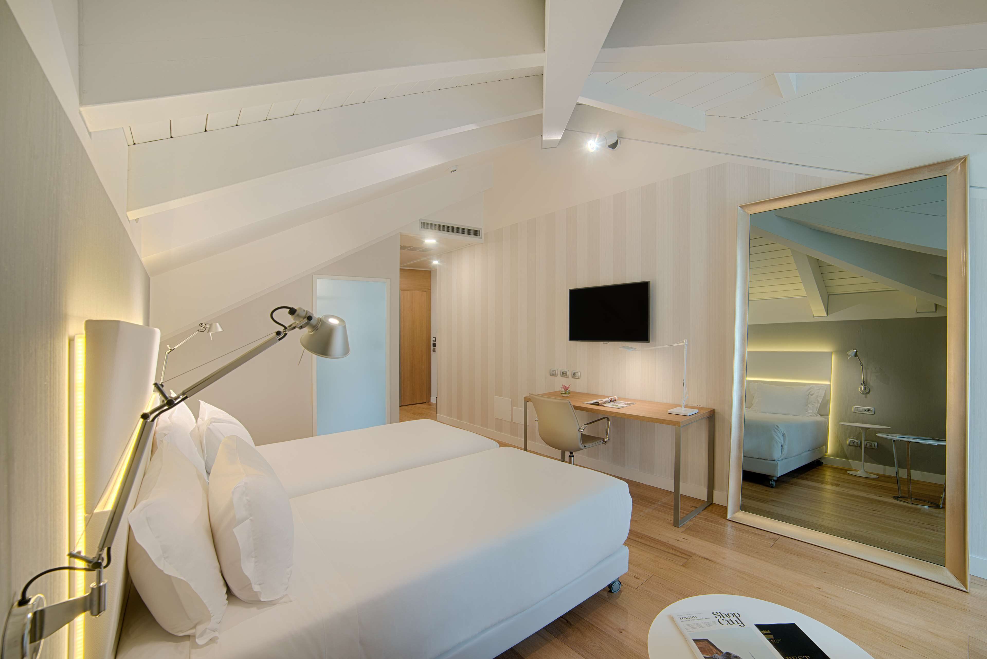 Una habitación de hotel moderna con una cama grande, un escritorio, un televisor de pantalla plana y un espejo.