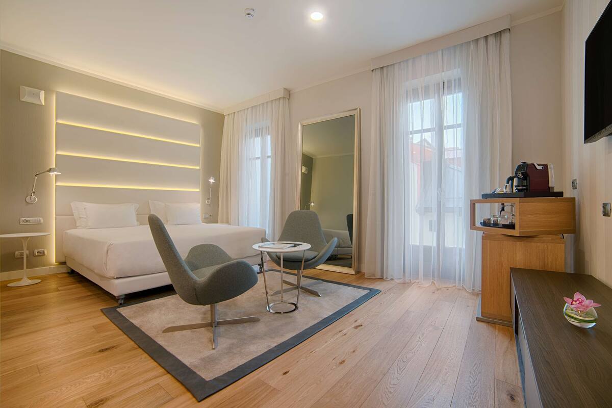 Ein modernes Hotelzimmer mit einem Bett, zwei Stühlen, einem kleinen Tisch und einem Fernseher.