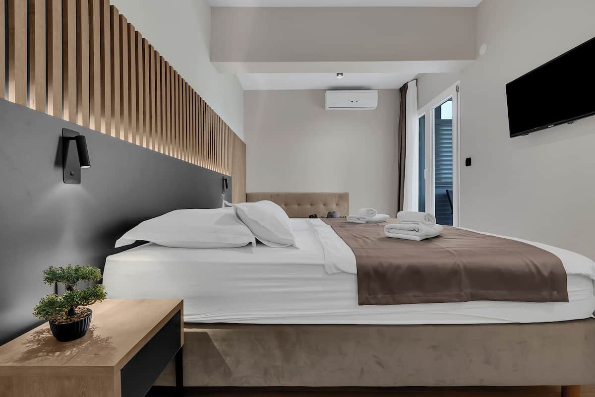 A modern hotel room with a bed, bedside table, potted plant, and a mounted TV.