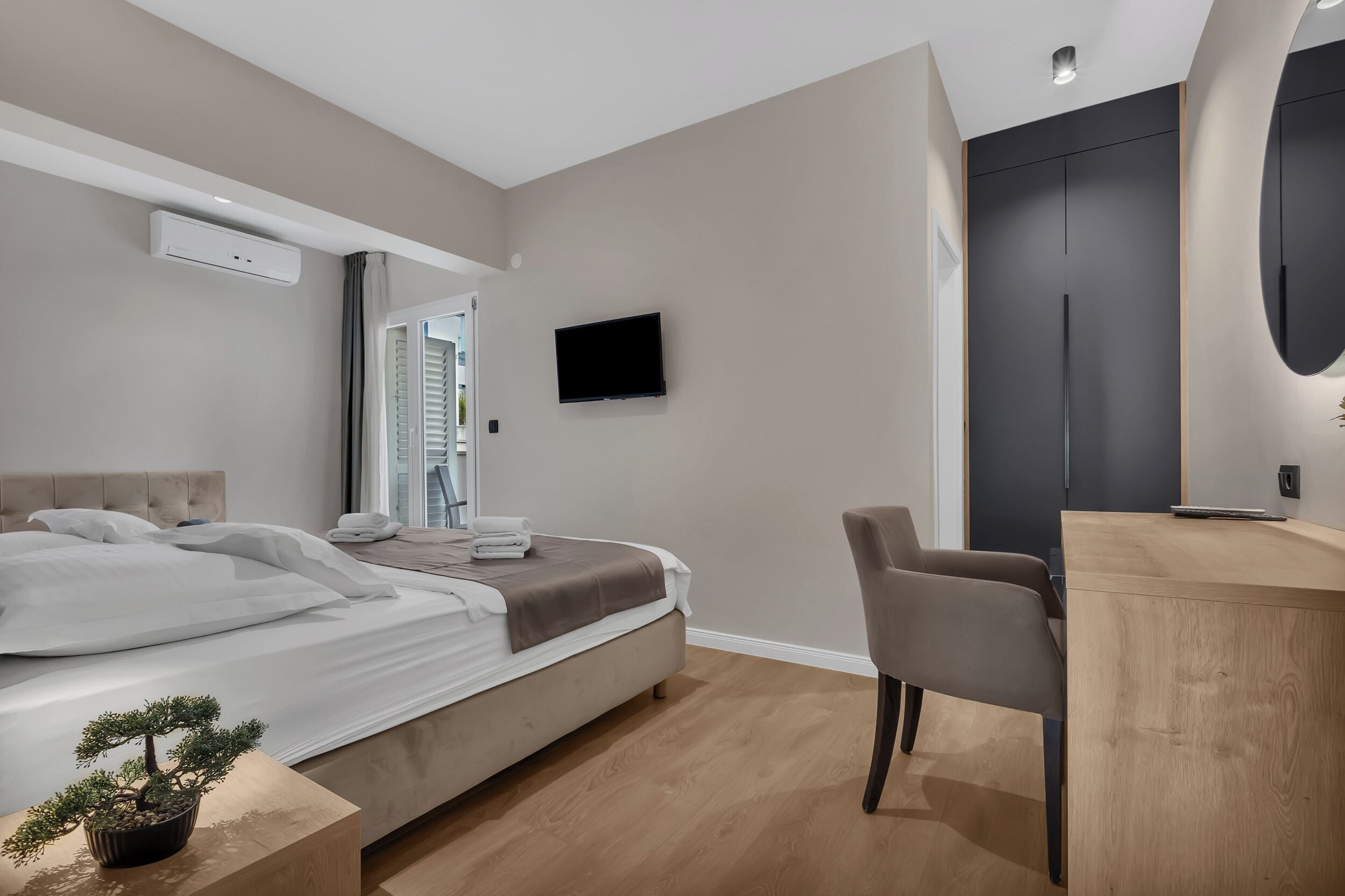 A modern hotel room with a bed, a desk, a chair, a TV, and an air conditioning unit.
