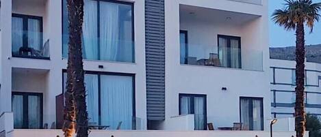 A modern multi-story hotel with balconies, large windows, and a pool area.
