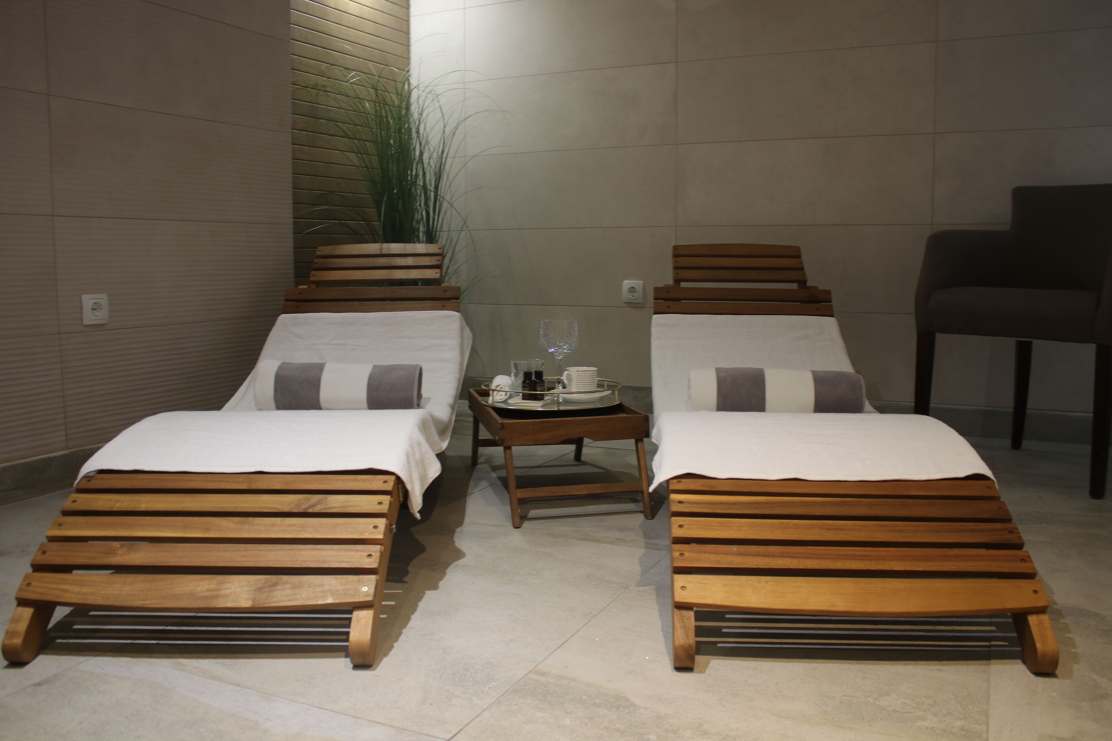 Duas camas de madeira com roupa de cama branca, uma mesa pequena com um tabuleiro de objetos e uma planta em vaso.