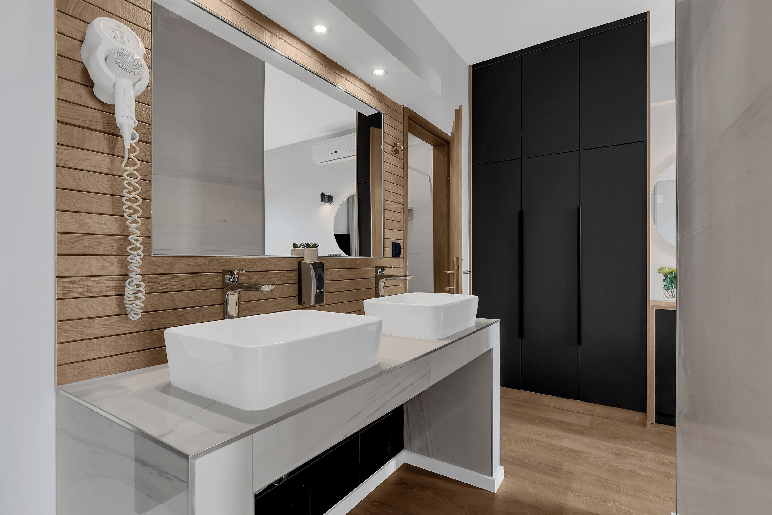 A modern bathroom with two white sinks, a large mirror, and a hairdryer mounted on the wall.