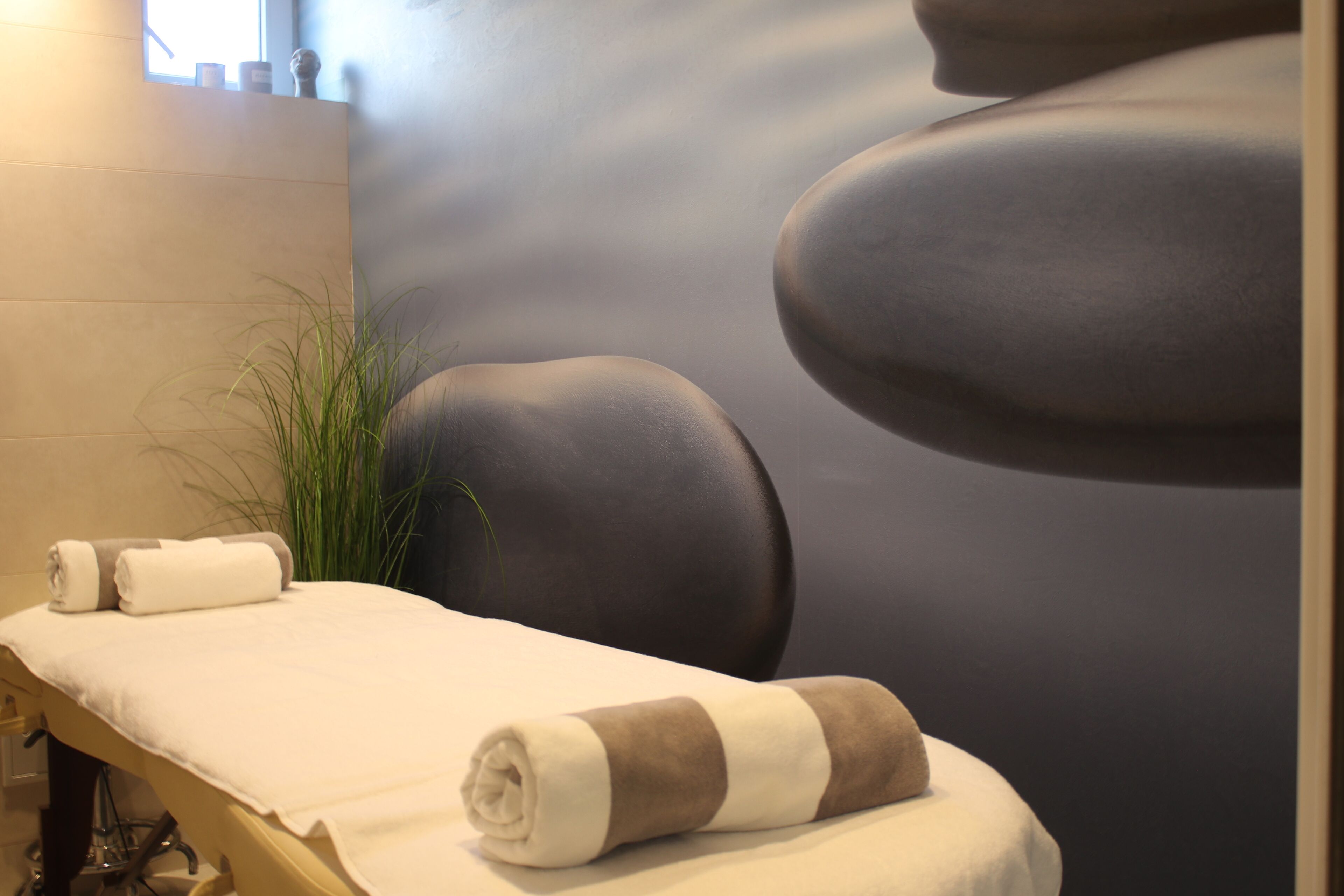 A spa treatment area with a massage table, towels, and a wall with a calming design.