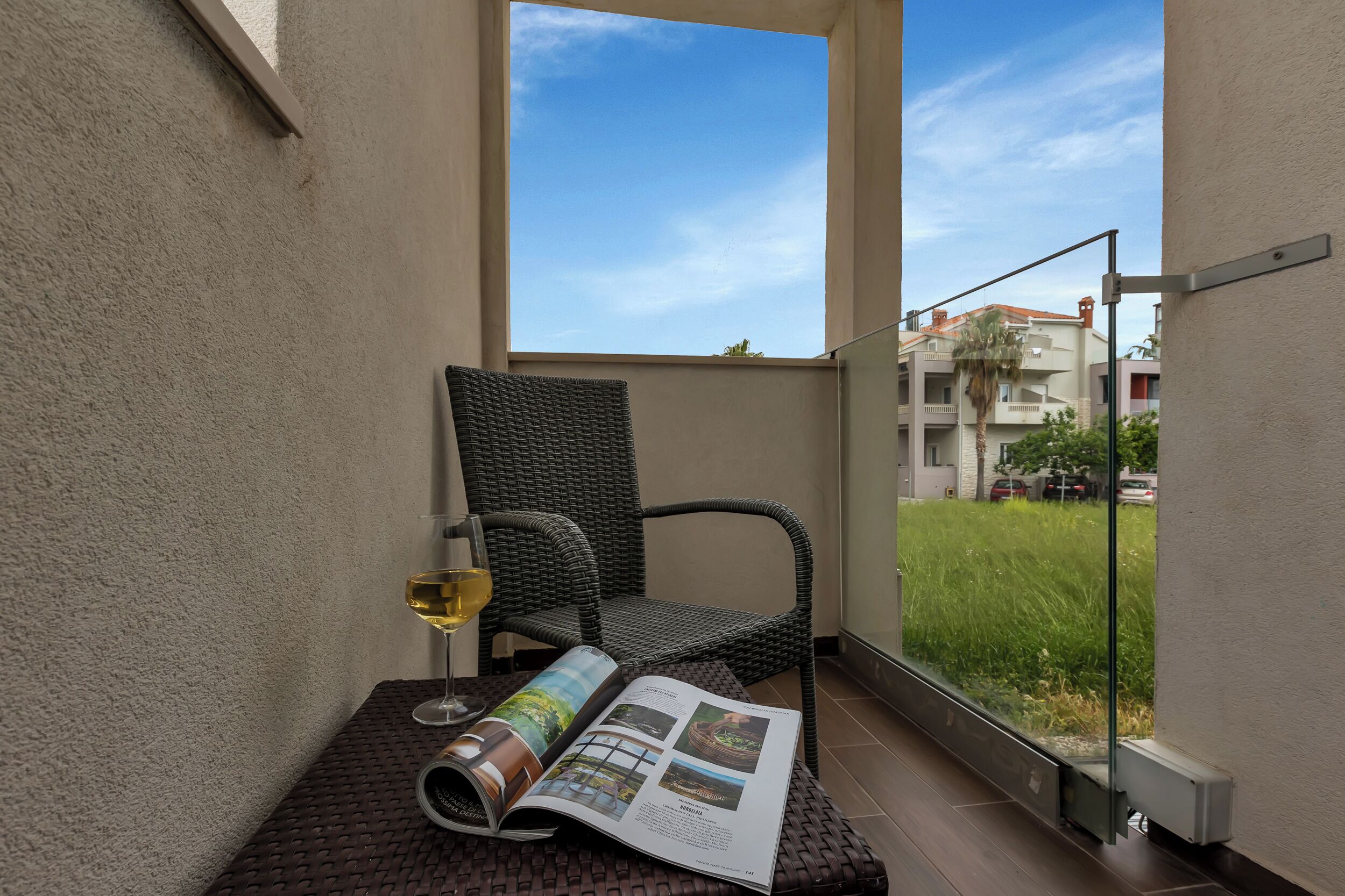 Een balkon met een rieten stoel, een glas wijn en een tijdschrift.