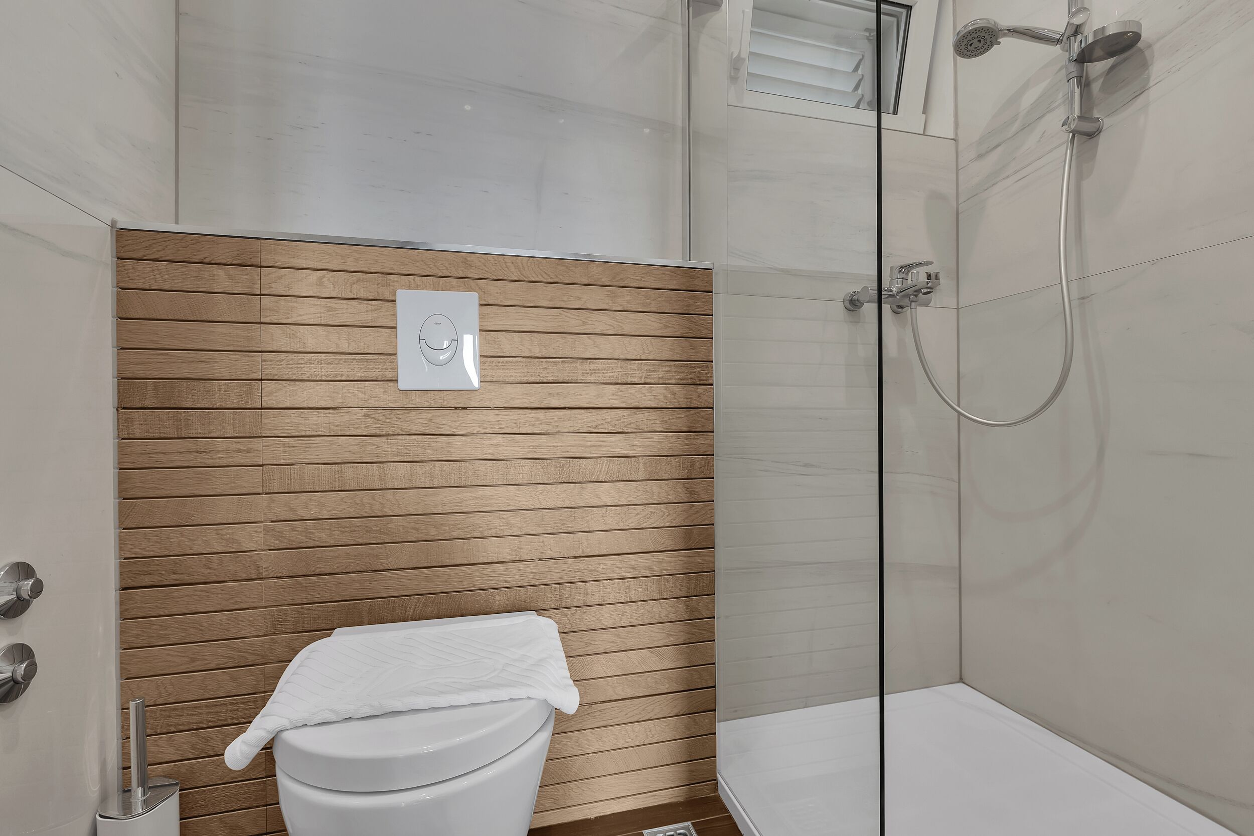A modern bathroom with a wooden panel wall, a white toilet, and a glass-enclosed shower area.