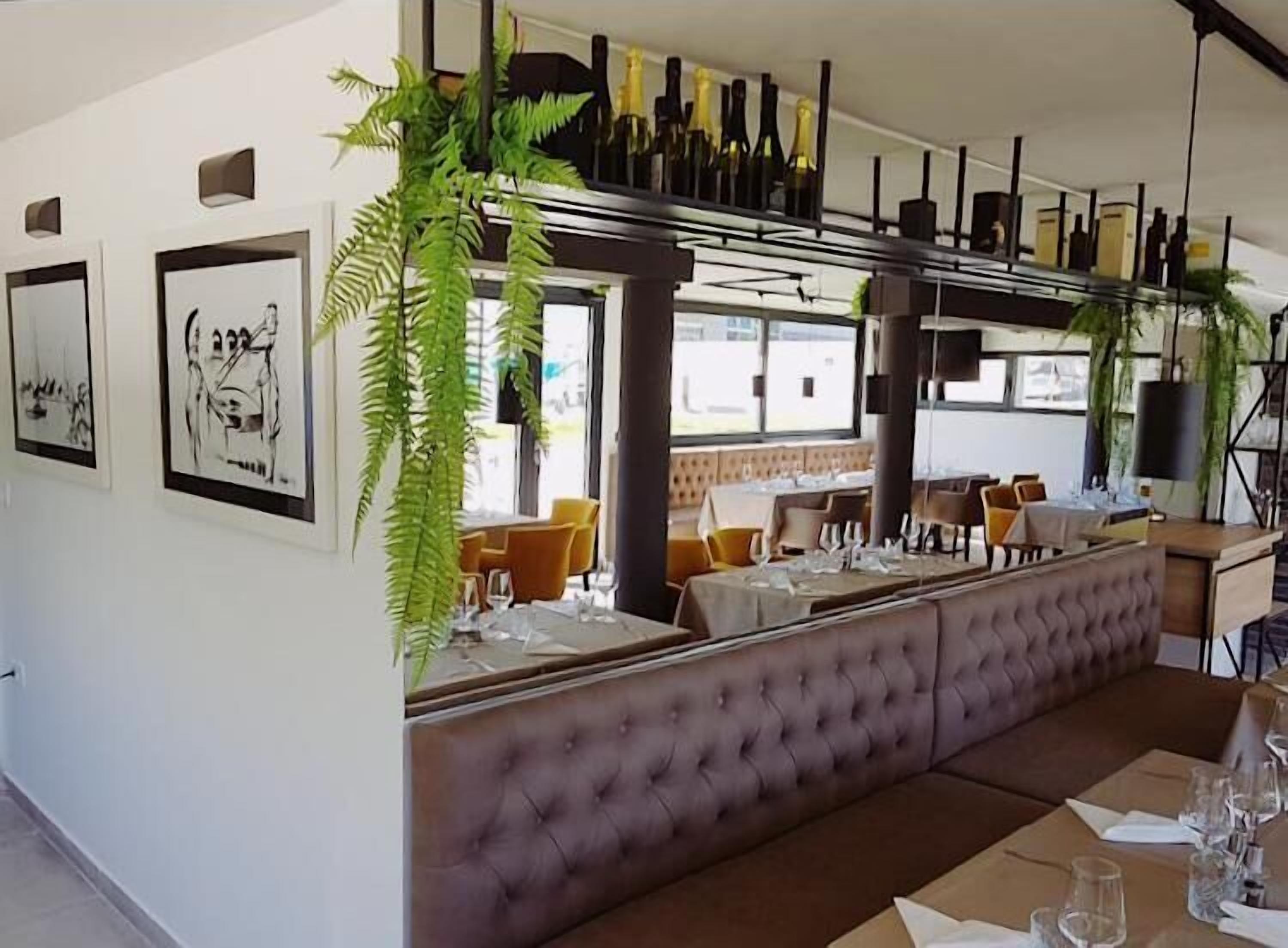 Ein Restaurantinnenraum mit einer langen Theke, gepolsterten Sitzgelegenheiten, gerahmten Kunstwerken an den Wänden und hängenden Pflanzen.